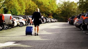 A parking lot with rows of parked cars and a person walking with a suitcase.