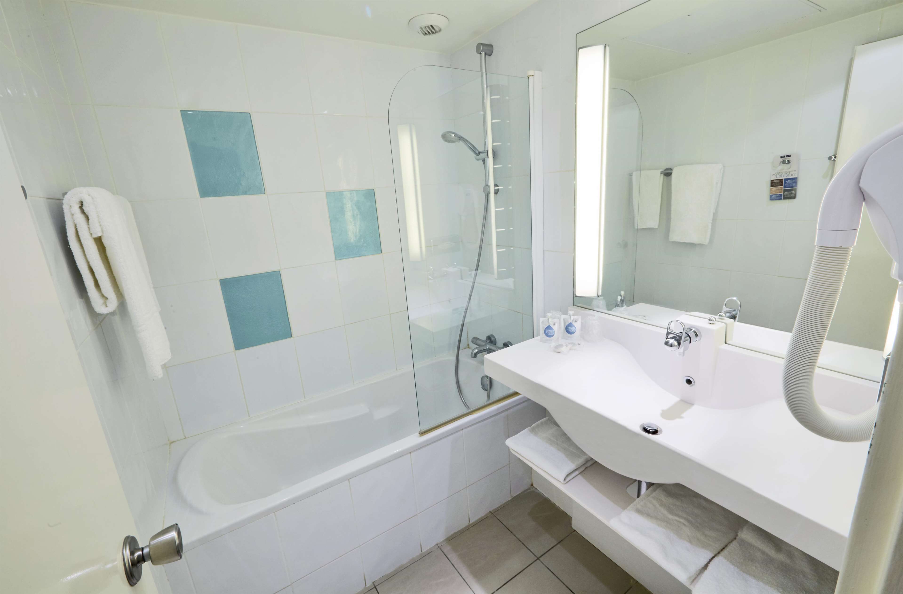 Un bagno moderno con doccia vetrata, lavandino bianco con specchio e portasciamani.