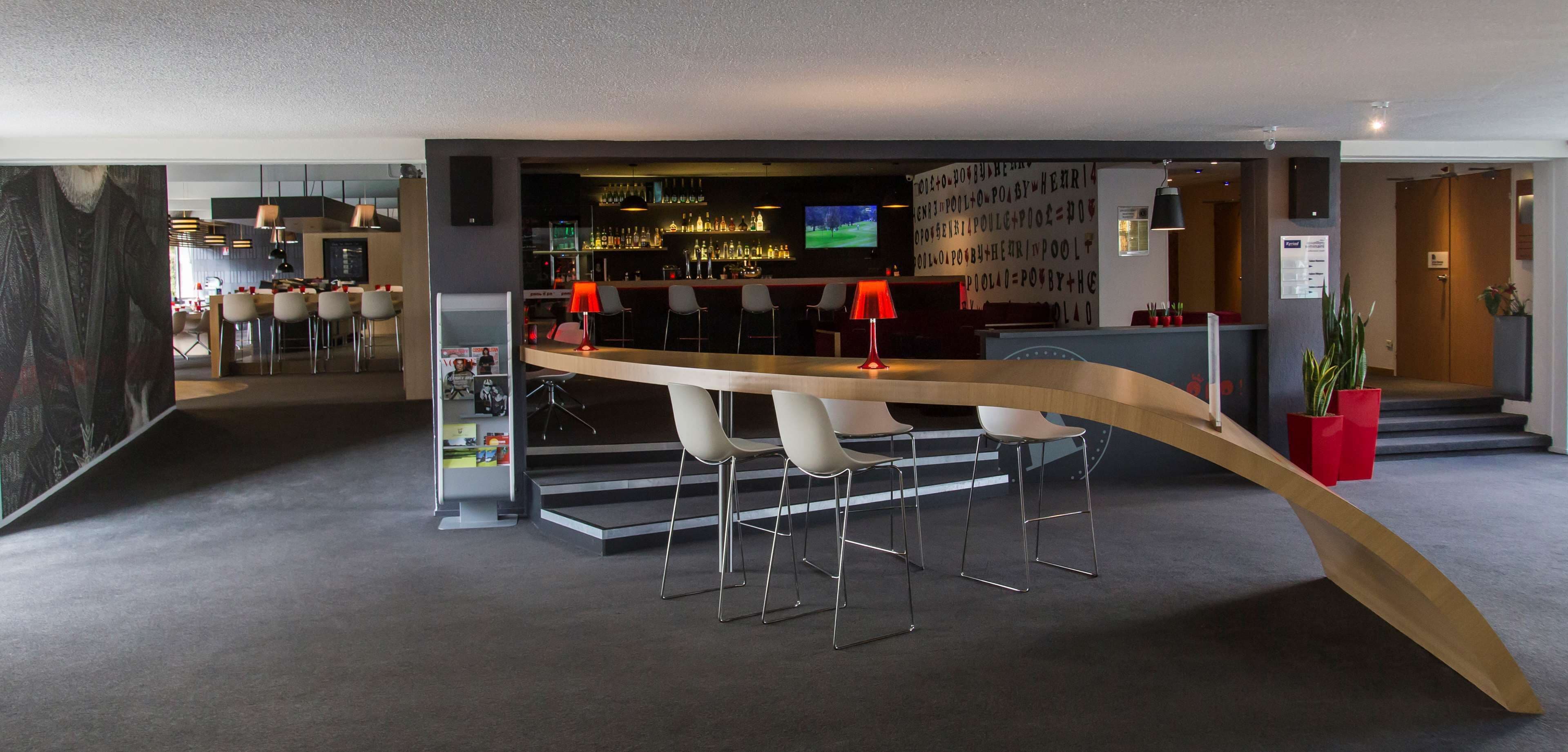 Un espace bar moderne doté d’un comptoir incurvé, de tabourets de bar et d’un écran de télévision.