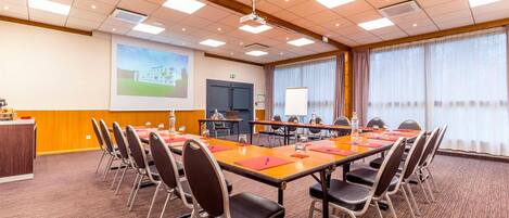 A conference room with a long table, chairs, a projector screen, and a large window with curtains.