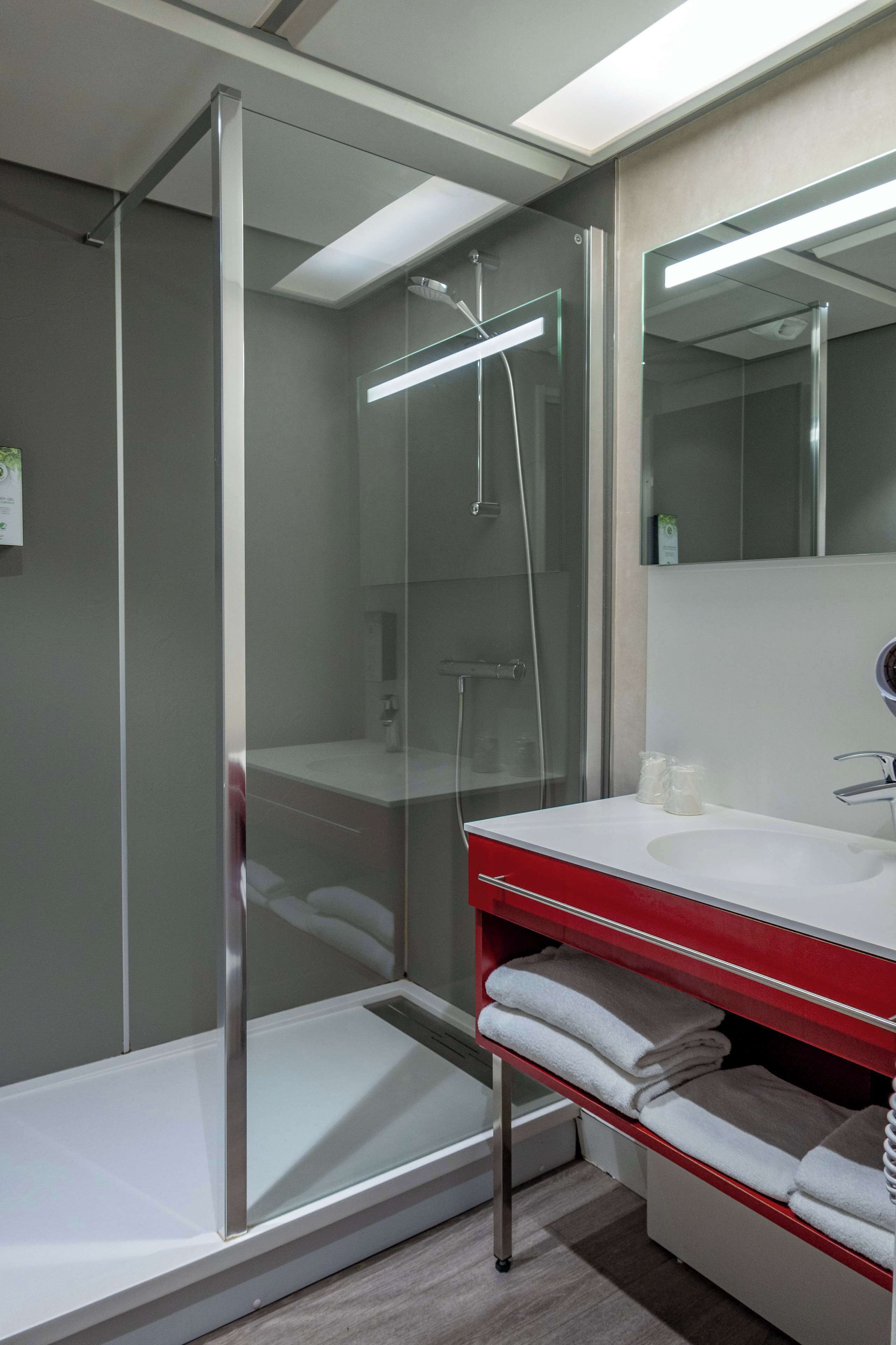 A modern bathroom with a glass-enclosed shower, a white sink with a red countertop, and a mirror above the sink.