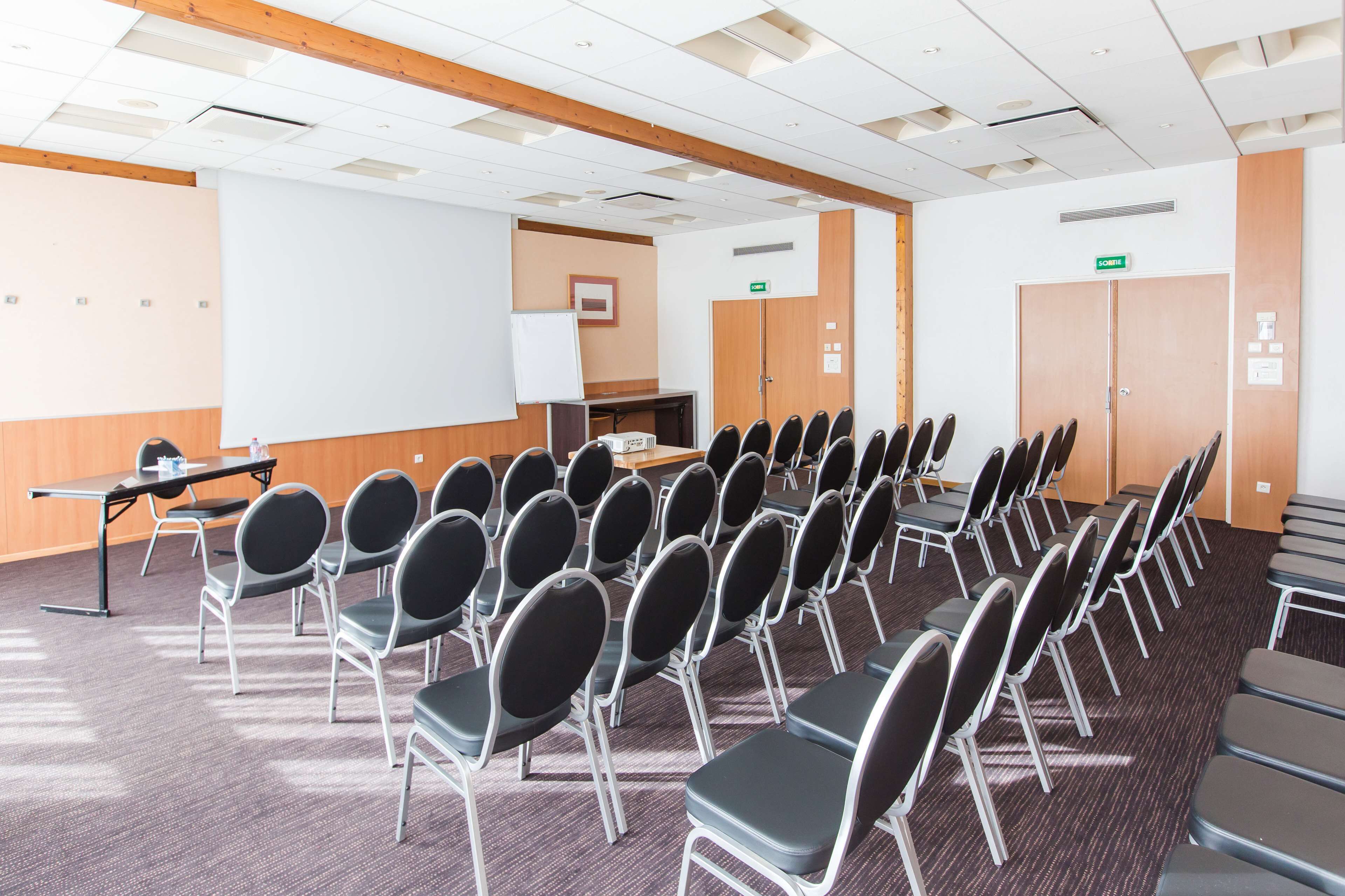 Una sala de conferencias con filas de sillas, una pizarra, una mesa con una computadora portátil y una puerta con un letrero.