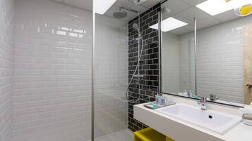 A modern bathroom with a glass-enclosed shower, white and black tiled walls, a white sink, and a yellow storage unit.