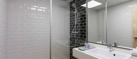 Un baño moderno con ducha de vidrio, paredes con azulejos blancos y negros, un lavamanos blanco y un almacenamiento amarillo.