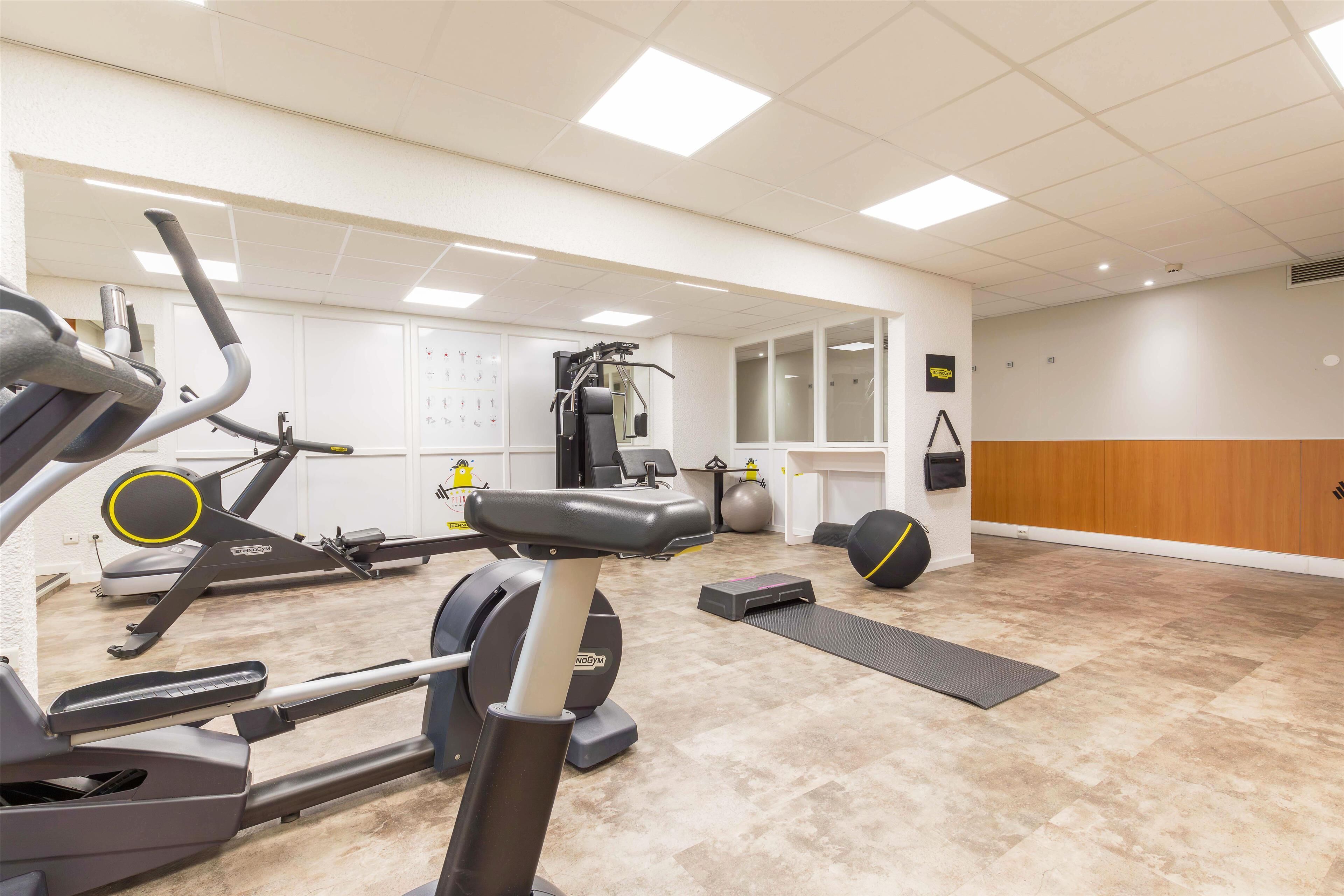Un gimnasio con máquinas de cardio, pesas libres y un espejo.
