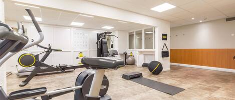 Un gimnasio con máquinas de cardio, pesas libres y un espejo.