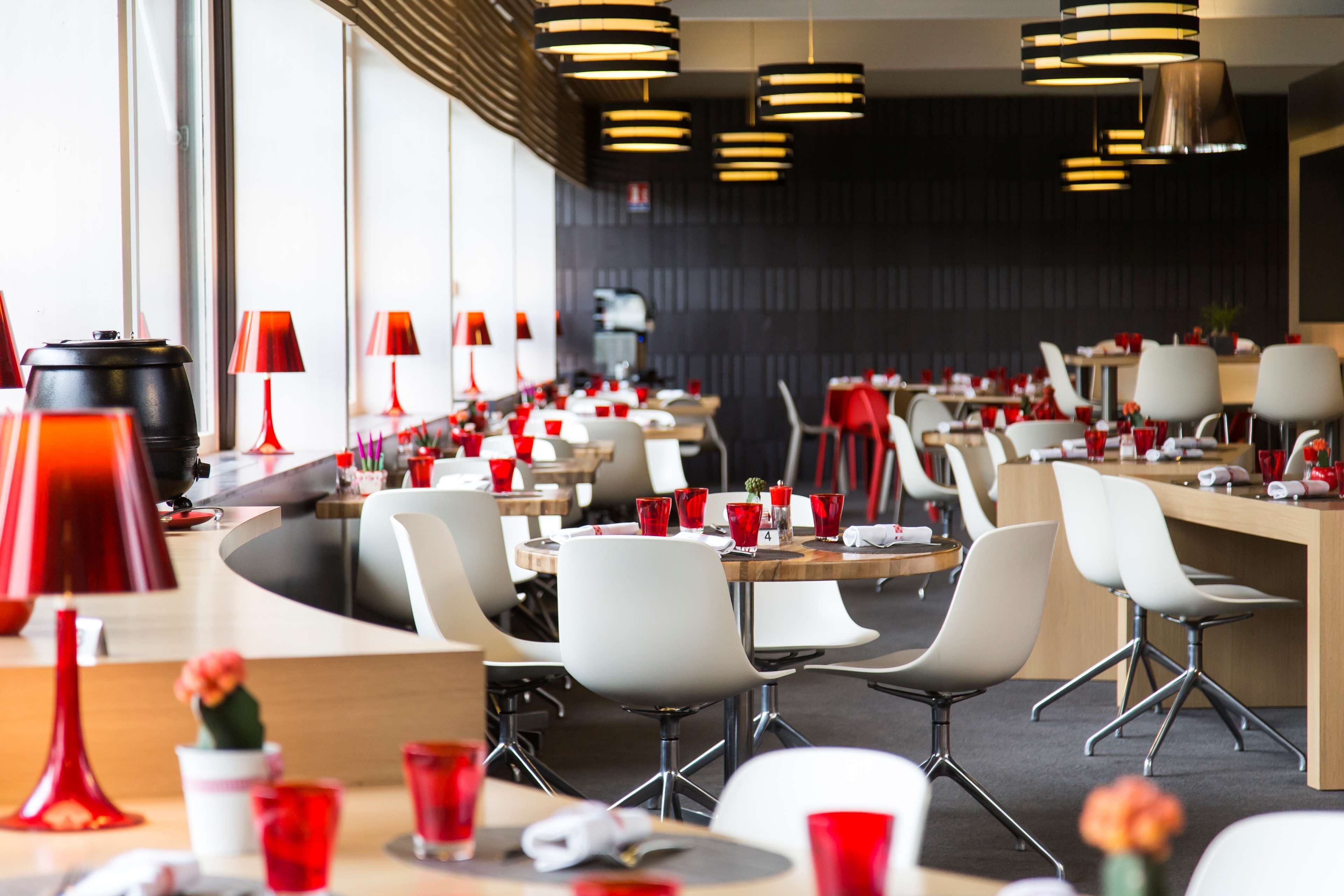 Ein modernes Restaurant mit weißen Stühlen, roten Tischlampen und einer langen Theke.