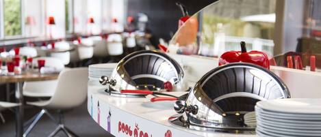 A modern restaurant with a curved counter, metal dishware, and a playful wall decoration.