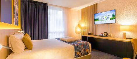 A hotel room with a bed, a desk, a television, and a window with curtains.