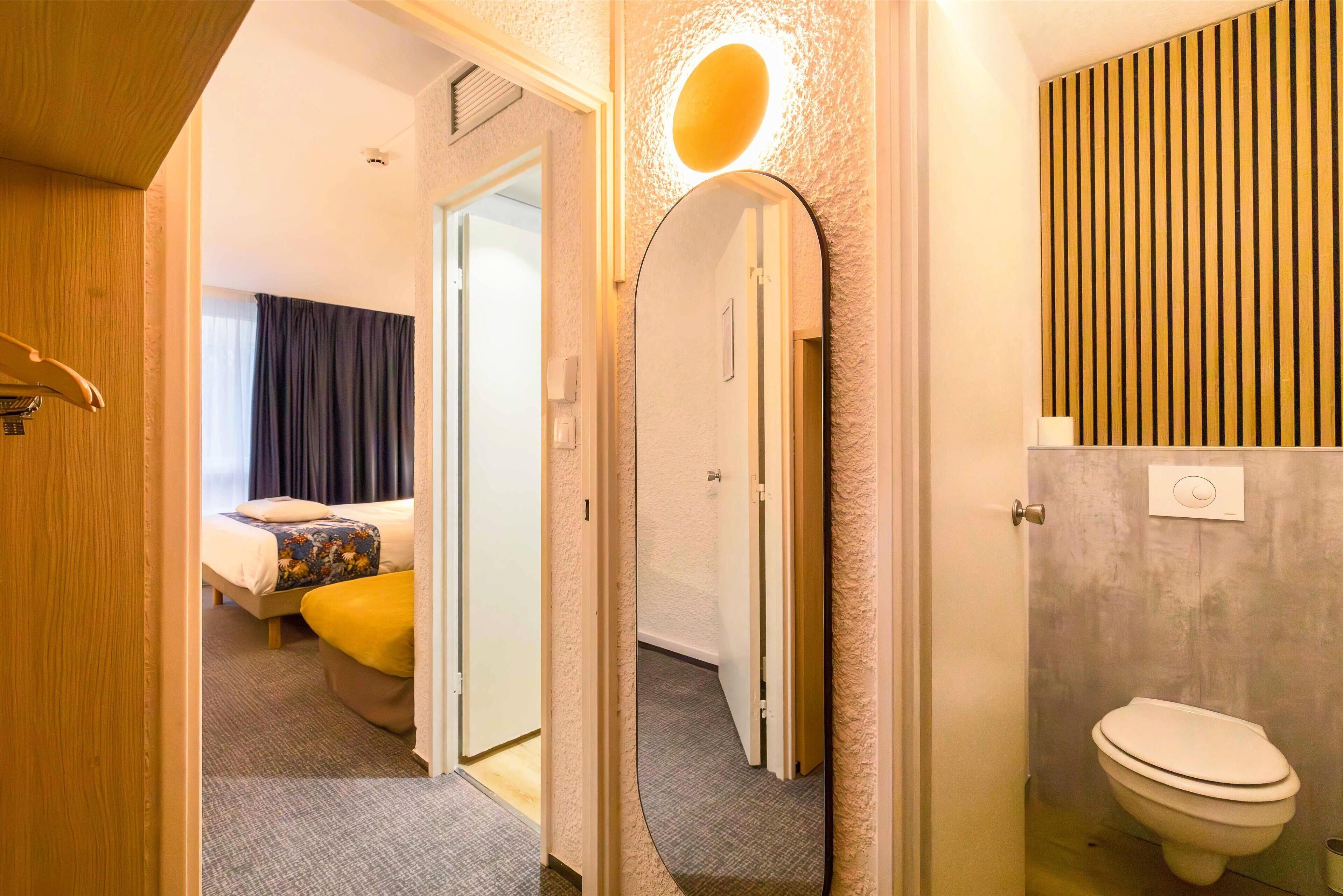 Habitació d'hotel amb un llit, un bany amb vàter i un mirall que reflecteix l'espai.