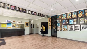 A reception area with framed pictures on the walls, a wooden floor, and a person in a yellow jacket standing near a door.