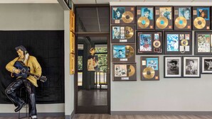 A room with a large mural of a man playing guitar, framed pictures on the wall, and a wooden floor.