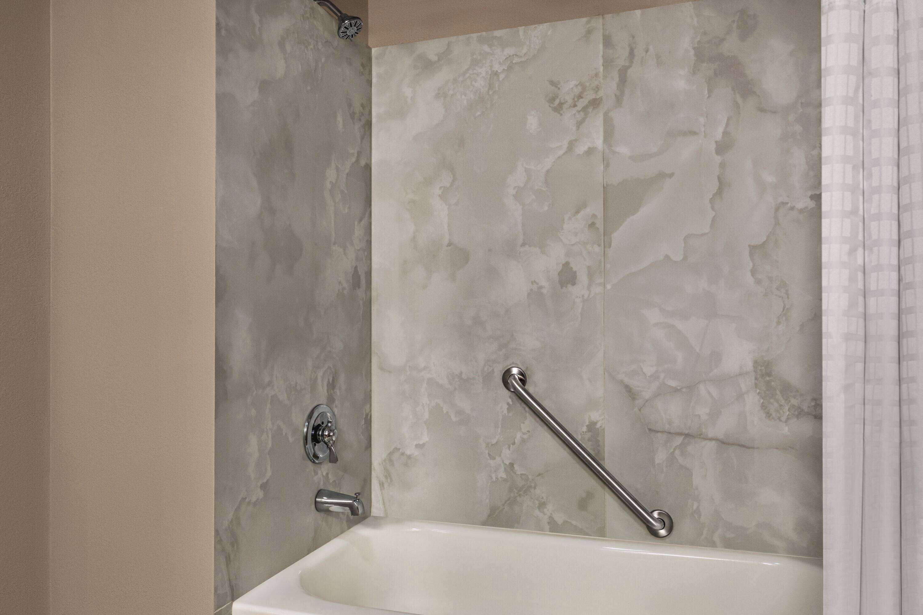 A bathroom with a bathtub, a shower, and a handrail.