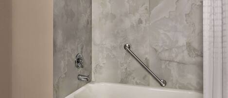 A bathroom with a bathtub, a shower, and a handrail.
