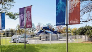 A fenced area with a blue and white airplane model, a white truck, and banners advertising Elvis Presley and Graceland.