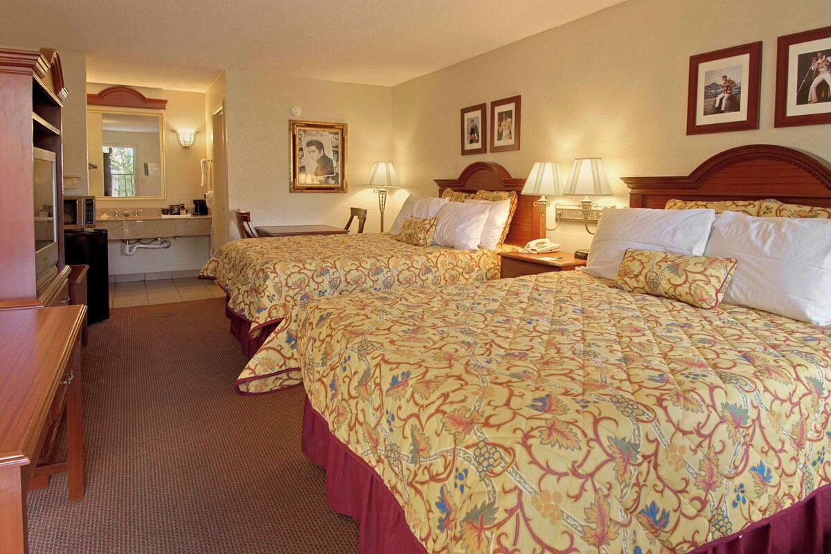 A hotel room with two beds, a desk, a chair, a vanity with a mirror, and a telephone.