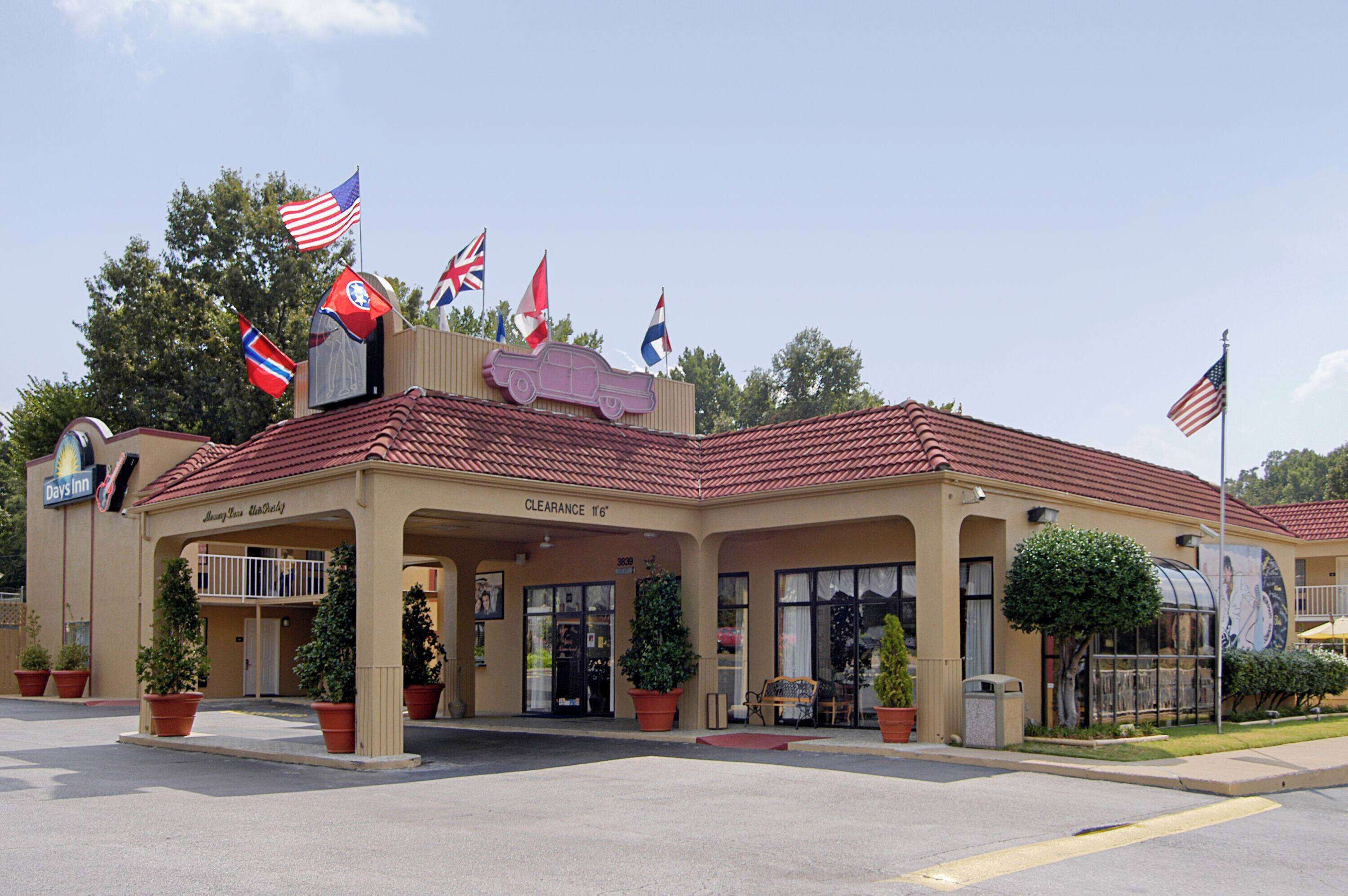 Un motel con techo de tejas rojas, varias banderas y una entrada despejada.