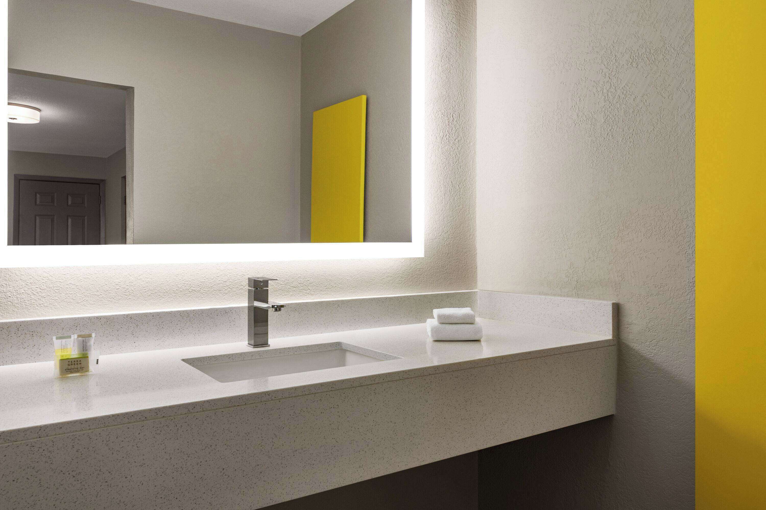 Un bany amb un lavabo blanc, un mirall i una paret de color groc.