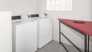 Una sala de bugaderia amb dues rentadores blanques, una taula vermella amb un rentatols i una finestra amb vidre decorat.