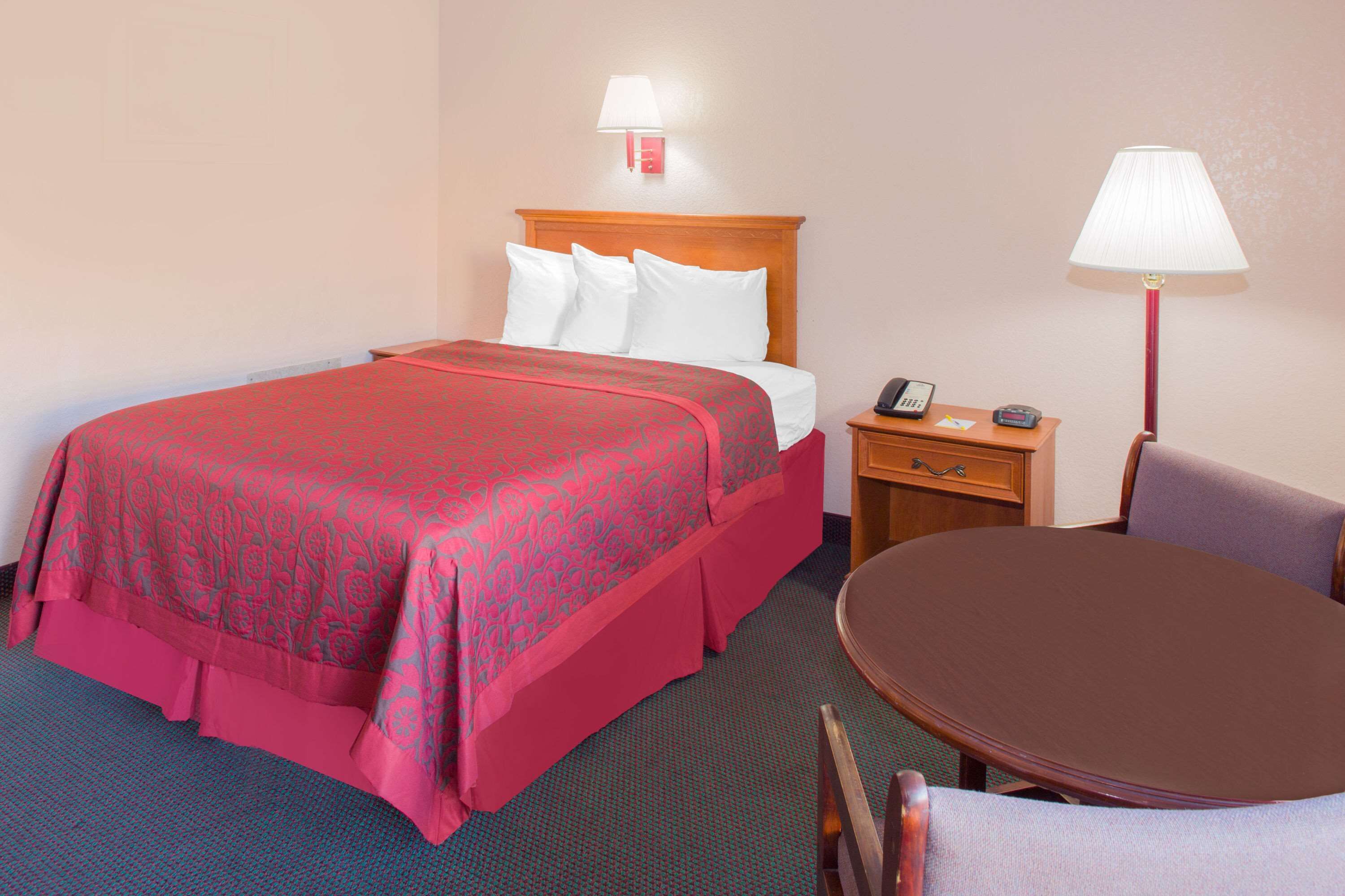 A hotel room with a bed, bedside table, lamp, and a round table with chairs.