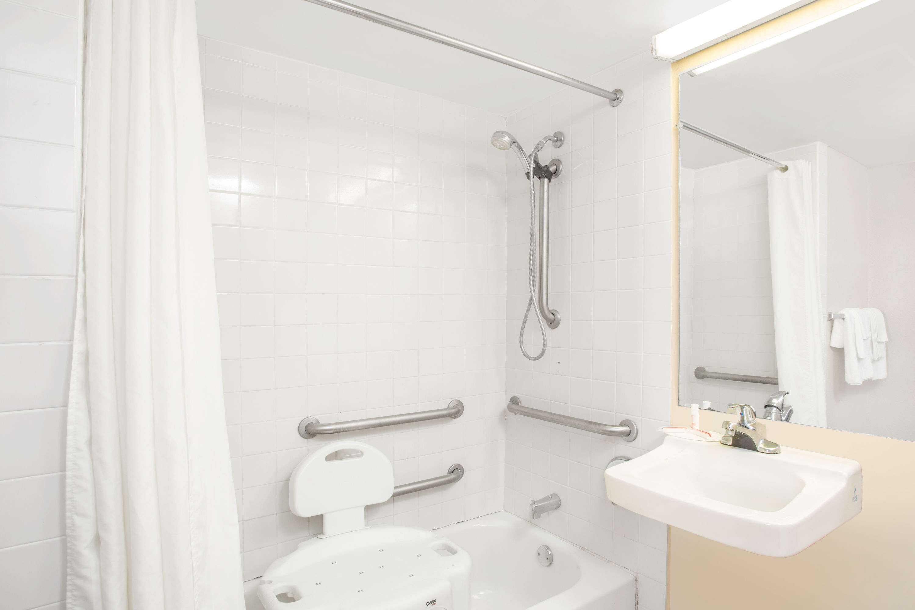 A bathroom with a white bathtub, a shower with a handheld showerhead, a sink with a mirror above it, and grab bars on the walls.