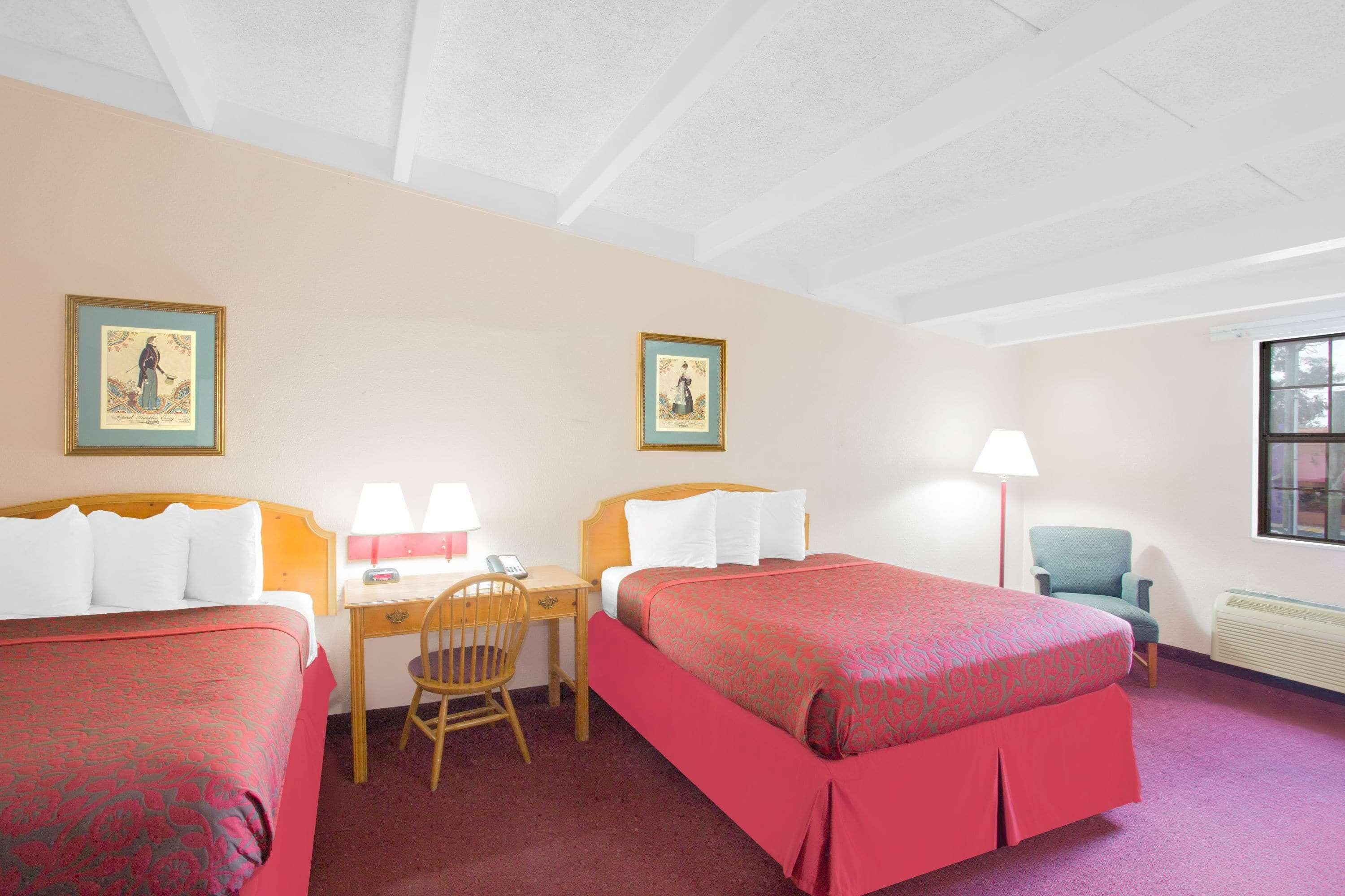 A hotel room with two beds, a desk, a chair, and two framed pictures on the wall.