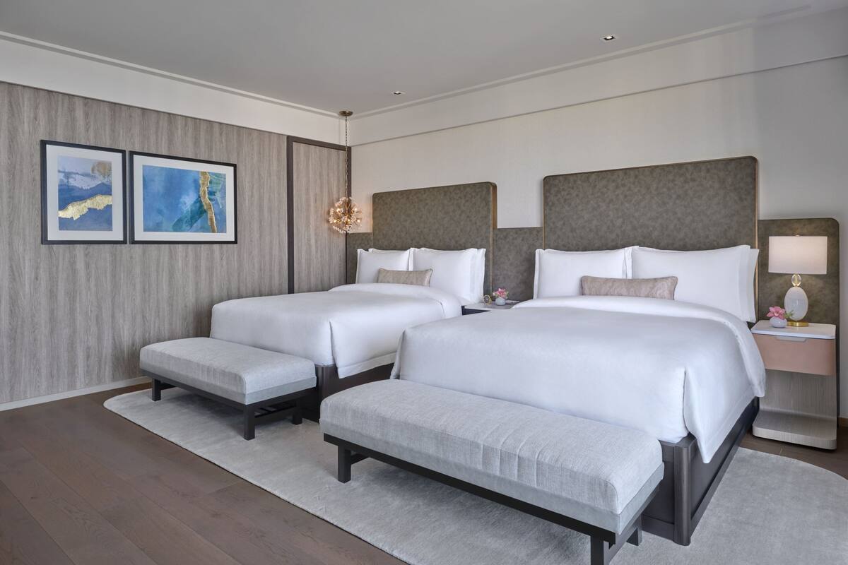 Ein Hotelzimmer mit zwei Betten, einem großen Spiegel, einem Nachttisch und zwei gerahmten Kunstwerken an der Wand.