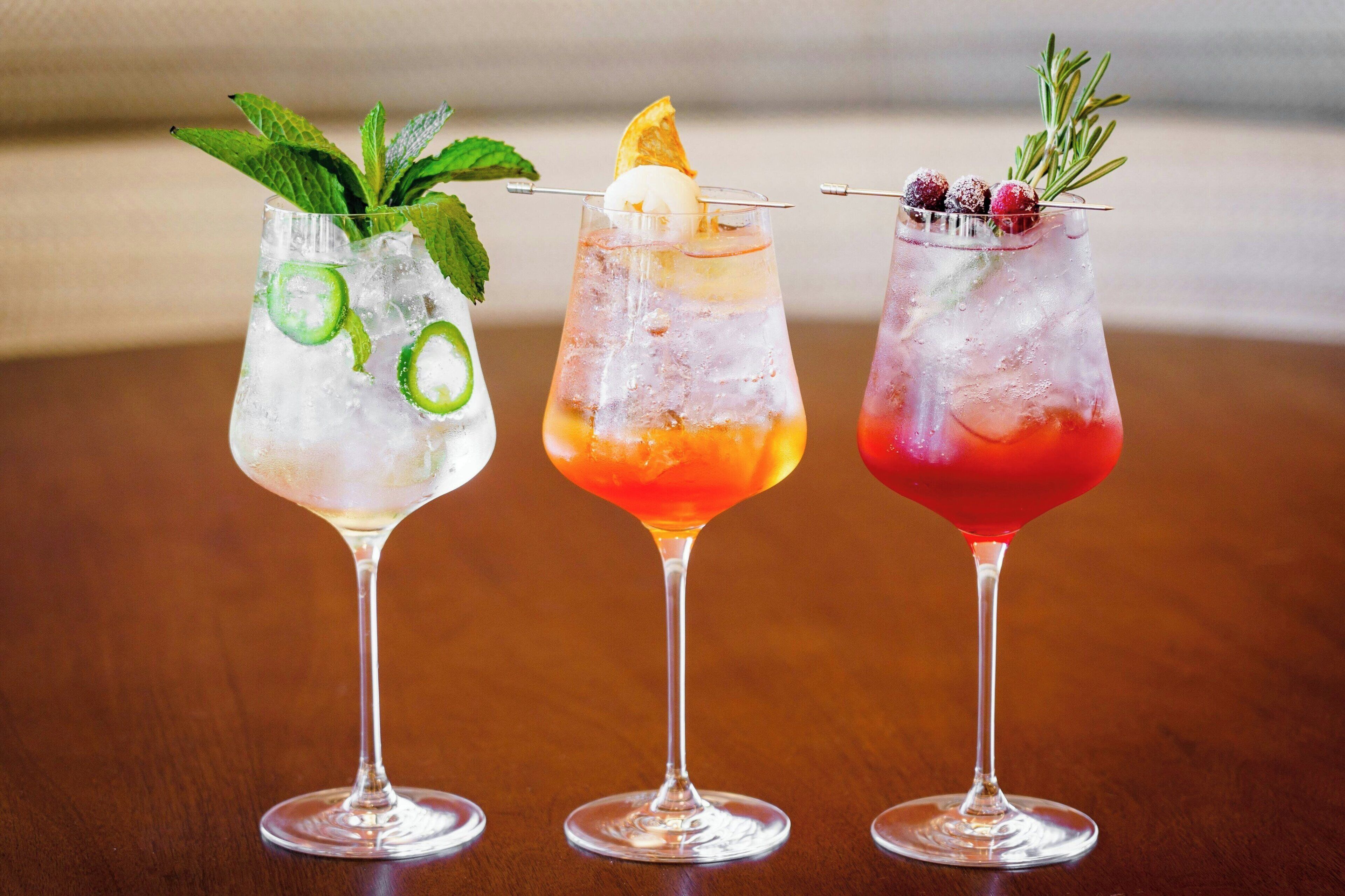 Tres cócteles en copas de martini, con hielo, adornos y un fondo desenfocado.