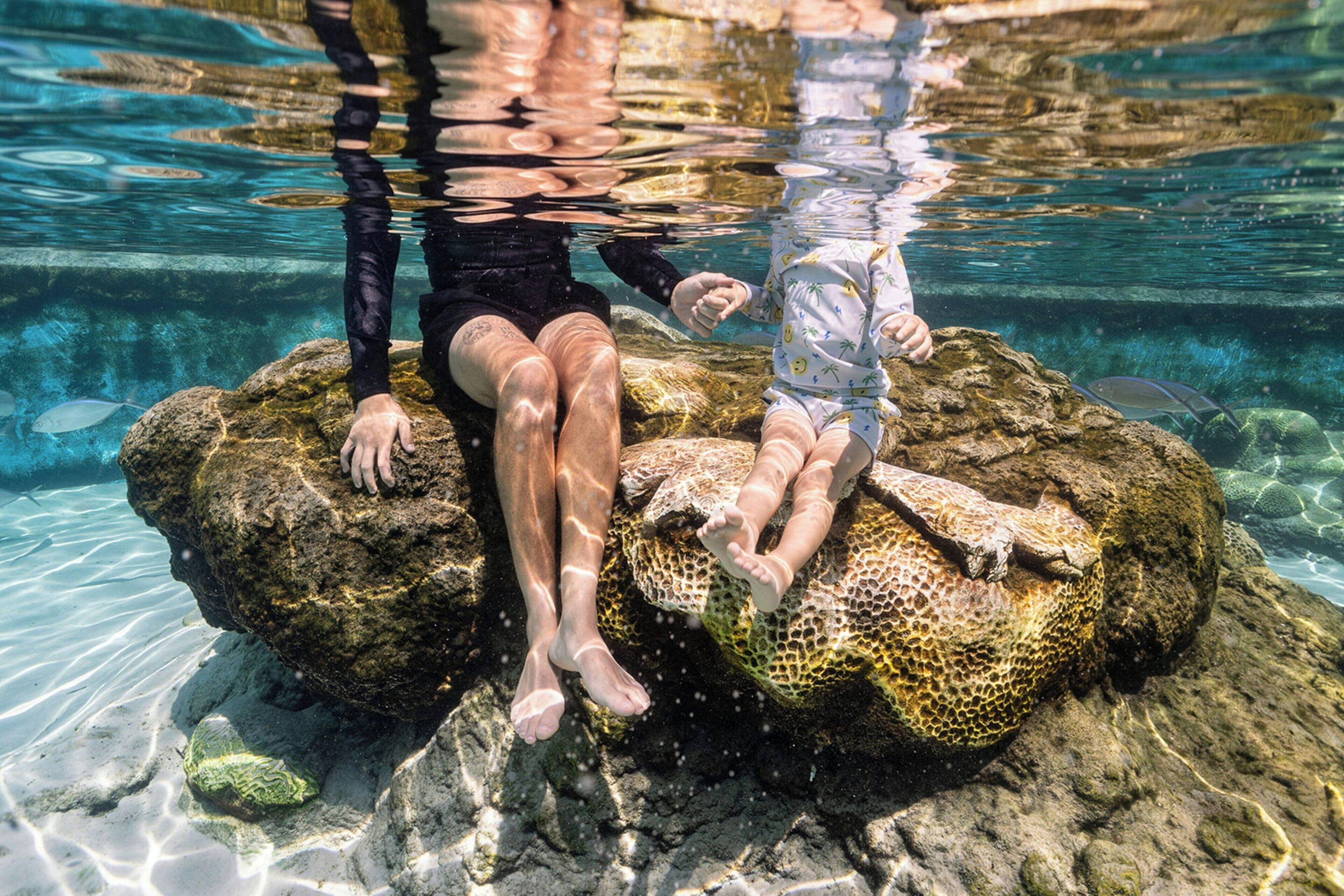 Two people sitting on a rock in clear water.
