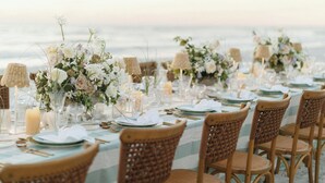 A beachside dining setup with wicker chairs and tables set for a meal, featuring floral centerpieces and candles. - The St. Regis Longboat Key Resort (Longboat Key)