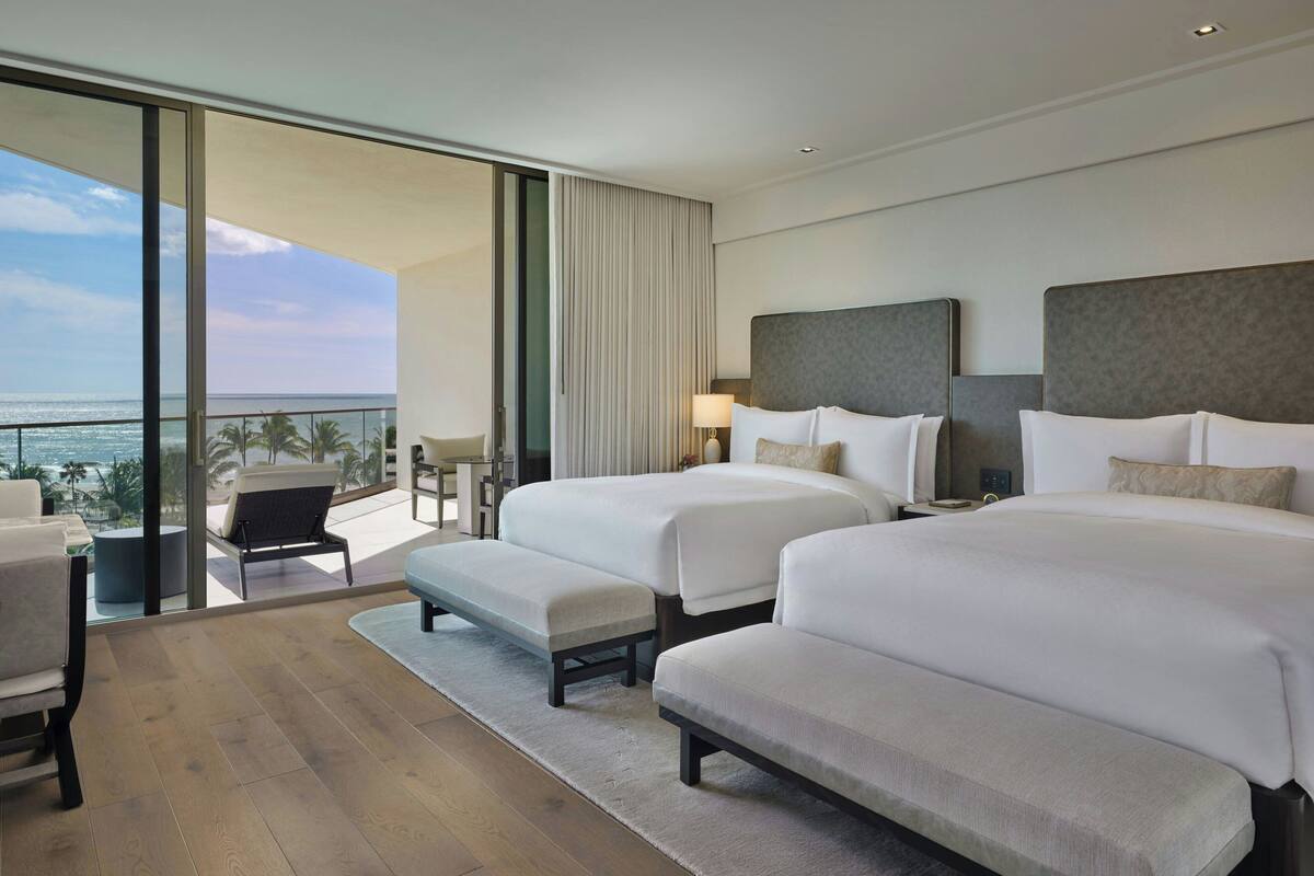 Ein Hotelzimmer mit zwei Betten, einem Schlafsofa, einem kleinen Tisch und Blick auf den Ozean.