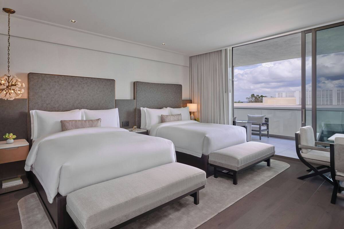 Ein modernes Hotelzimmer mit zwei Betten, einer Sitzecke und einem großen Fenster mit Blick auf die Stadt.