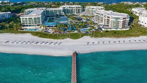 An aerial view of a resort with multiple buildings, a long pier extending into turquoise waters, and a beach with rows of umbrellas. - The St. Regis Longboat Key Resort (Longboat Key)