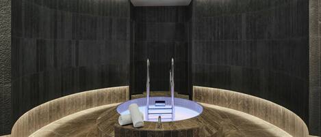 A modern spa with a circular hot tub, marble walls, and a ceiling with recessed lighting.