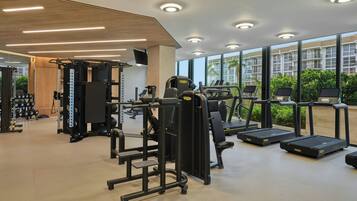 A modern gym with various exercise equipment, large windows, and a view of a residential area.