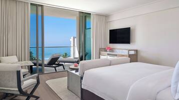 A modern hotel room with a large bed, a desk, a chair, and a balcony with a view of the ocean.