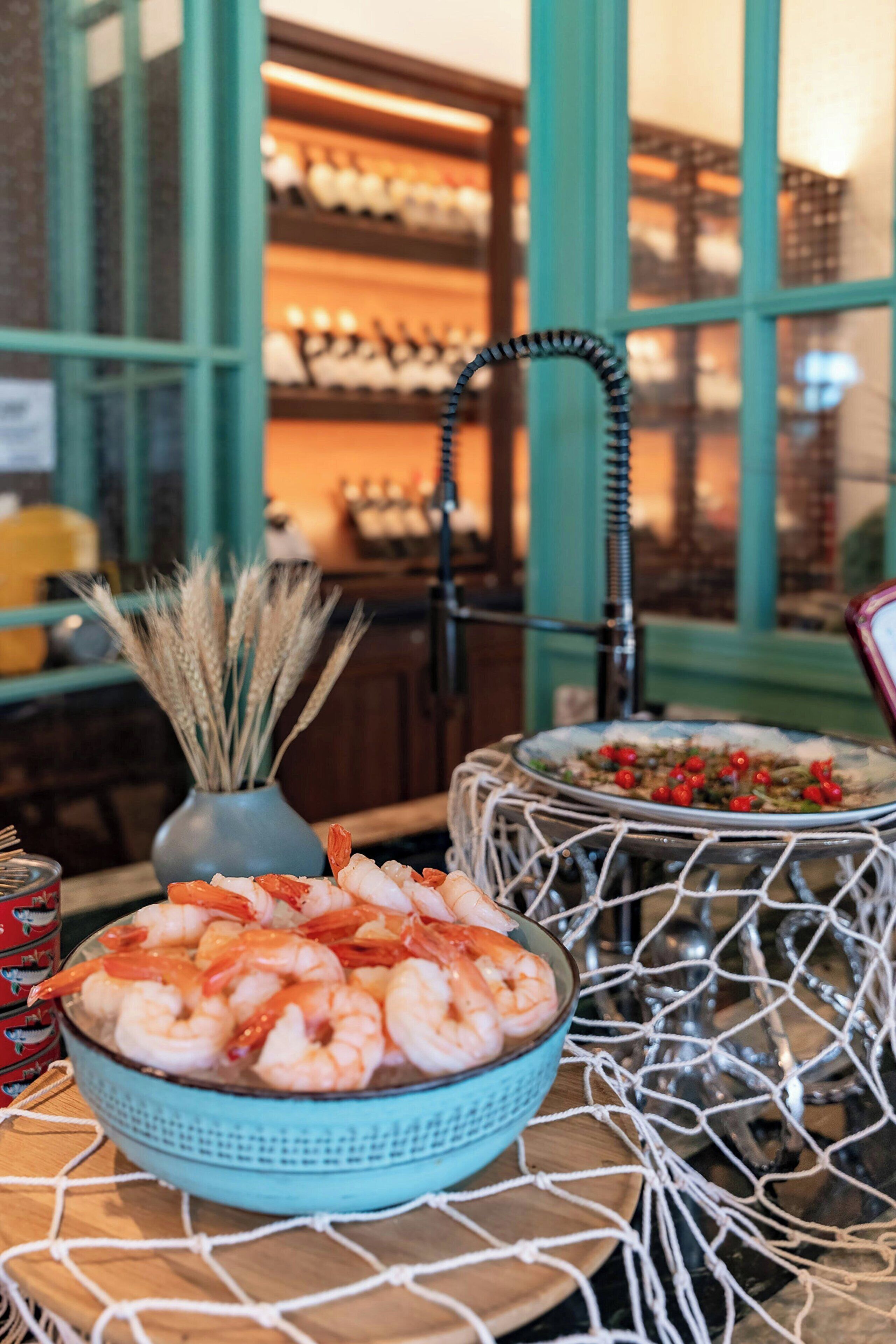 A table with a bowl of shrimp, a decorative vase with wheat stalks, and a bowl of food with red berries.