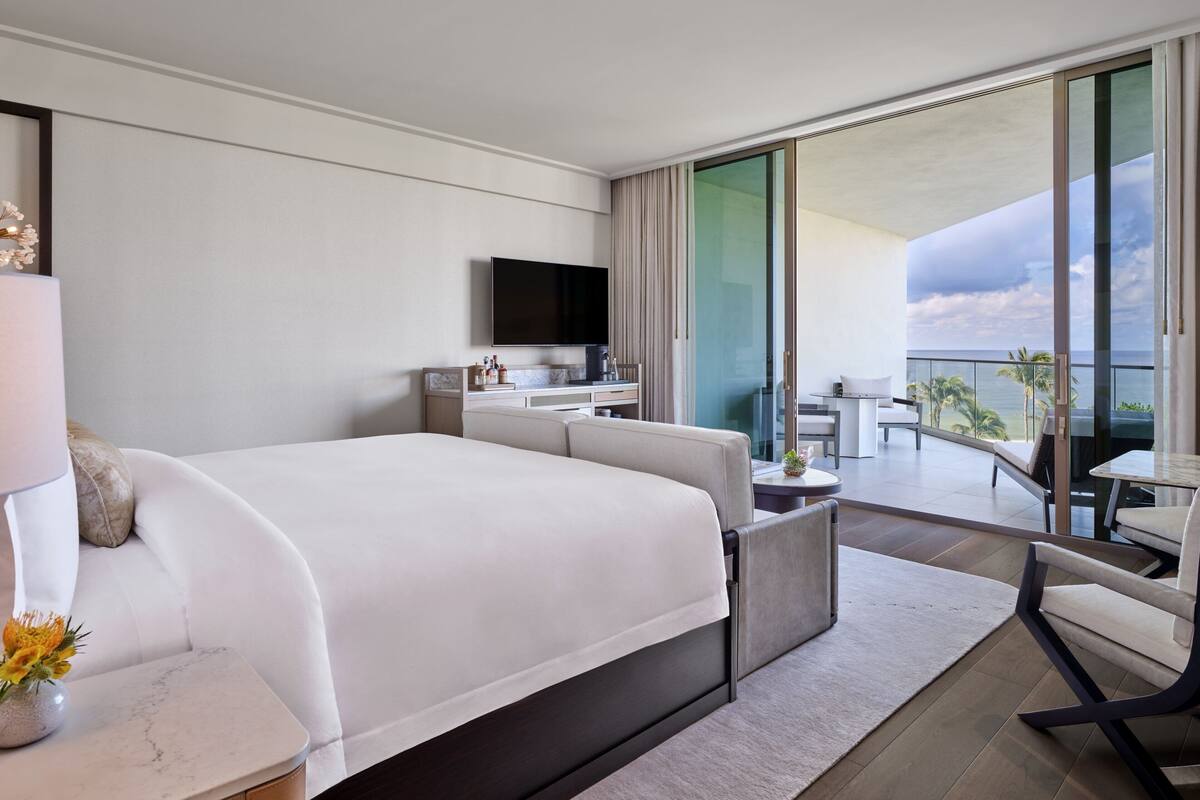 Ein modernes Hotelzimmer mit einem großen Bett, einem Flachbildfernseher, einem Balkon mit Meerblick und einer kleinen Sitzecke.