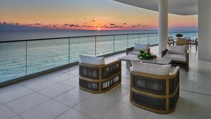 A balcony with wicker furniture, a table with a vase, and a view of the sunset over the ocean. - The St. Regis Longboat Key Resort (Longboat Key)