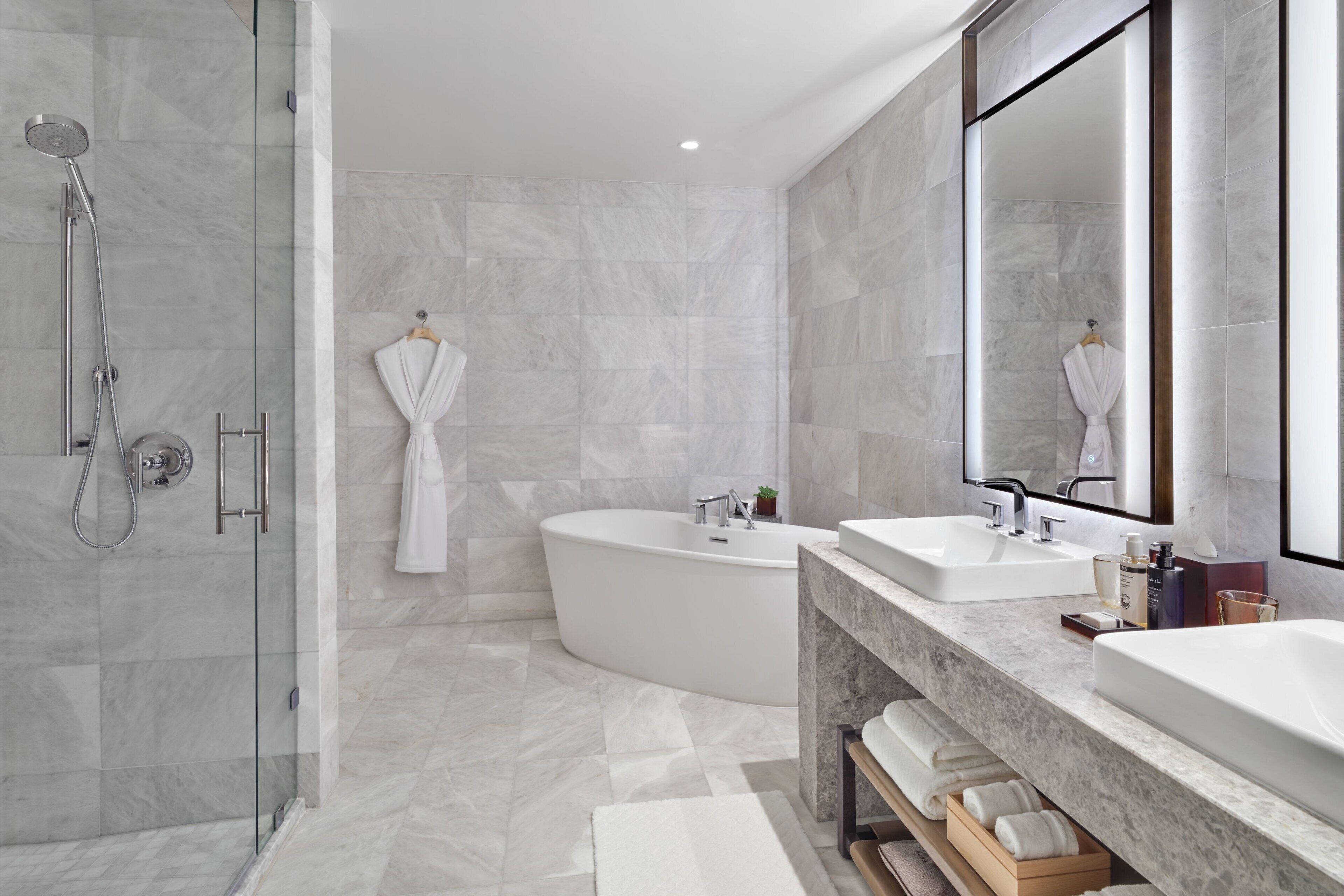 Un baño moderno con ducha envuelta en vidrio, una bañera independiente y un tocador con dos lavabos.