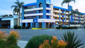 A multi-story hotel with a blue and white facade, palm trees, and a parking lot. - Capri Suites Anaheim (Anaheim)