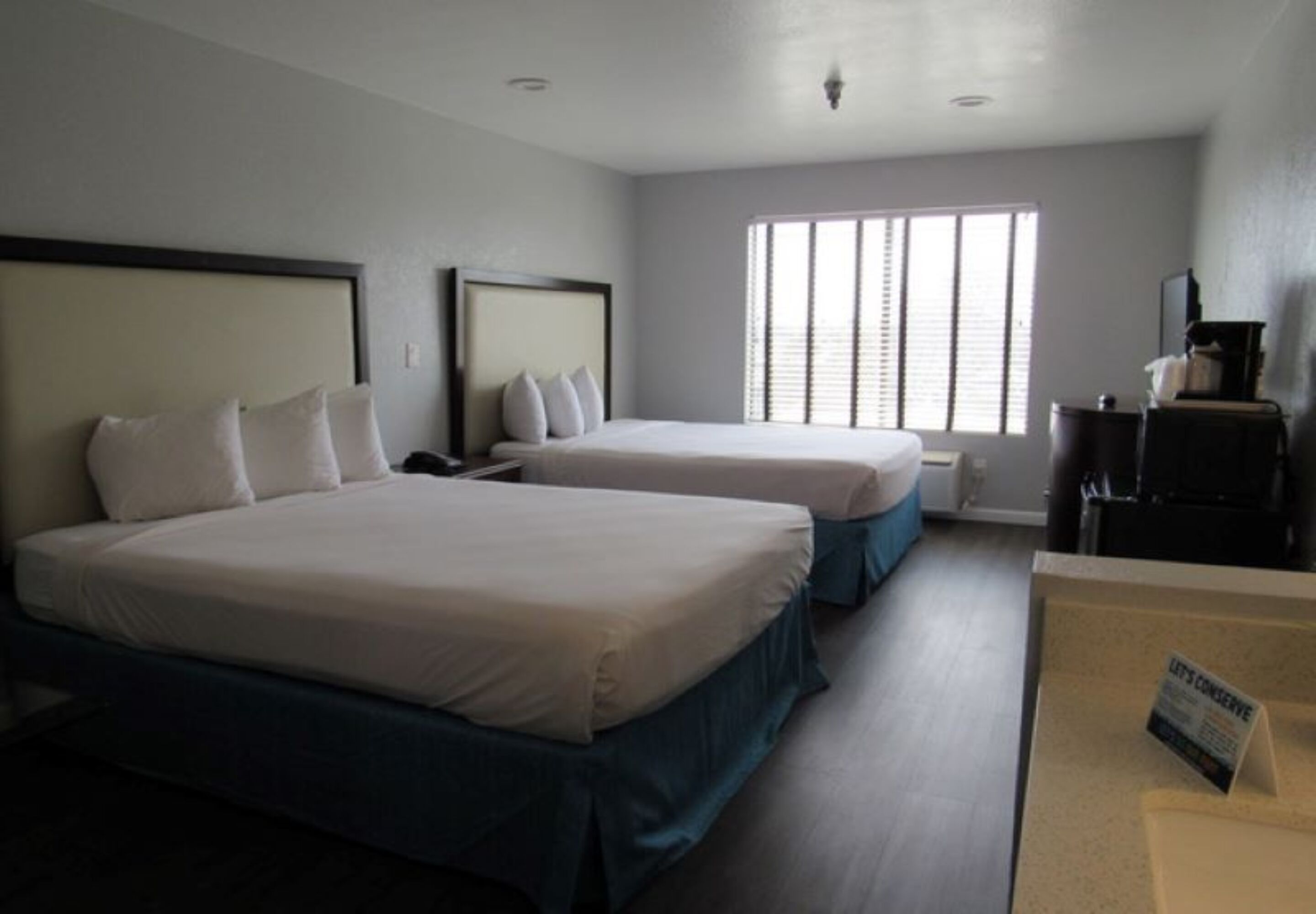 Ein Hotelzimmer mit zwei Betten, einem Schreibtisch und einem Fenster mit Jalousien.