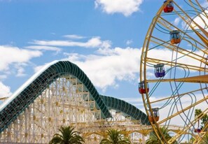 A roller coaster with a green track and a Ferris wheel in the foreground. - Capri Suites Anaheim (Anaheim)