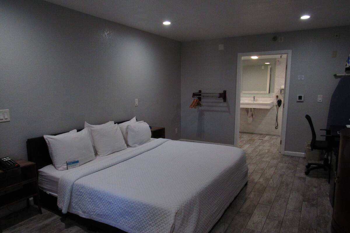 A bedroom with a large bed, a nightstand, a desk, and a bathroom visible through an open door.