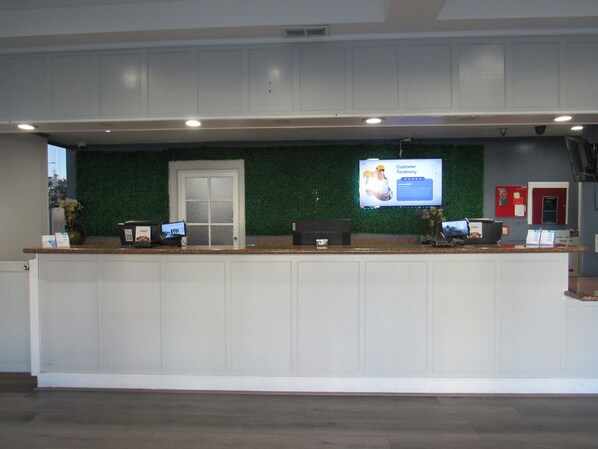 A reception desk with a green wall, a digital screen displaying a customer testimonial, and a door with a frosted glass panel.