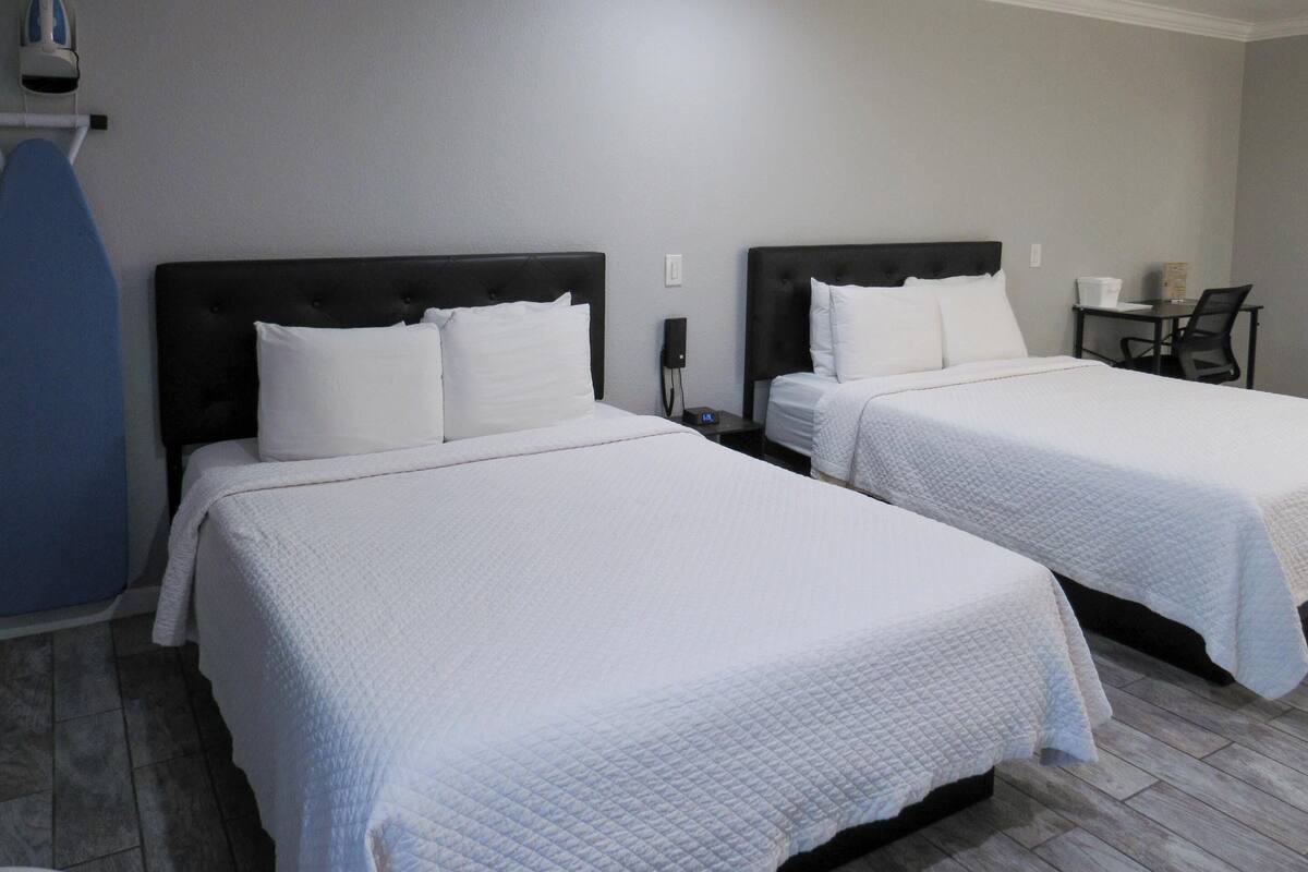 Two twin beds with white bedding, a small table with a chair, and a blue ironing board.