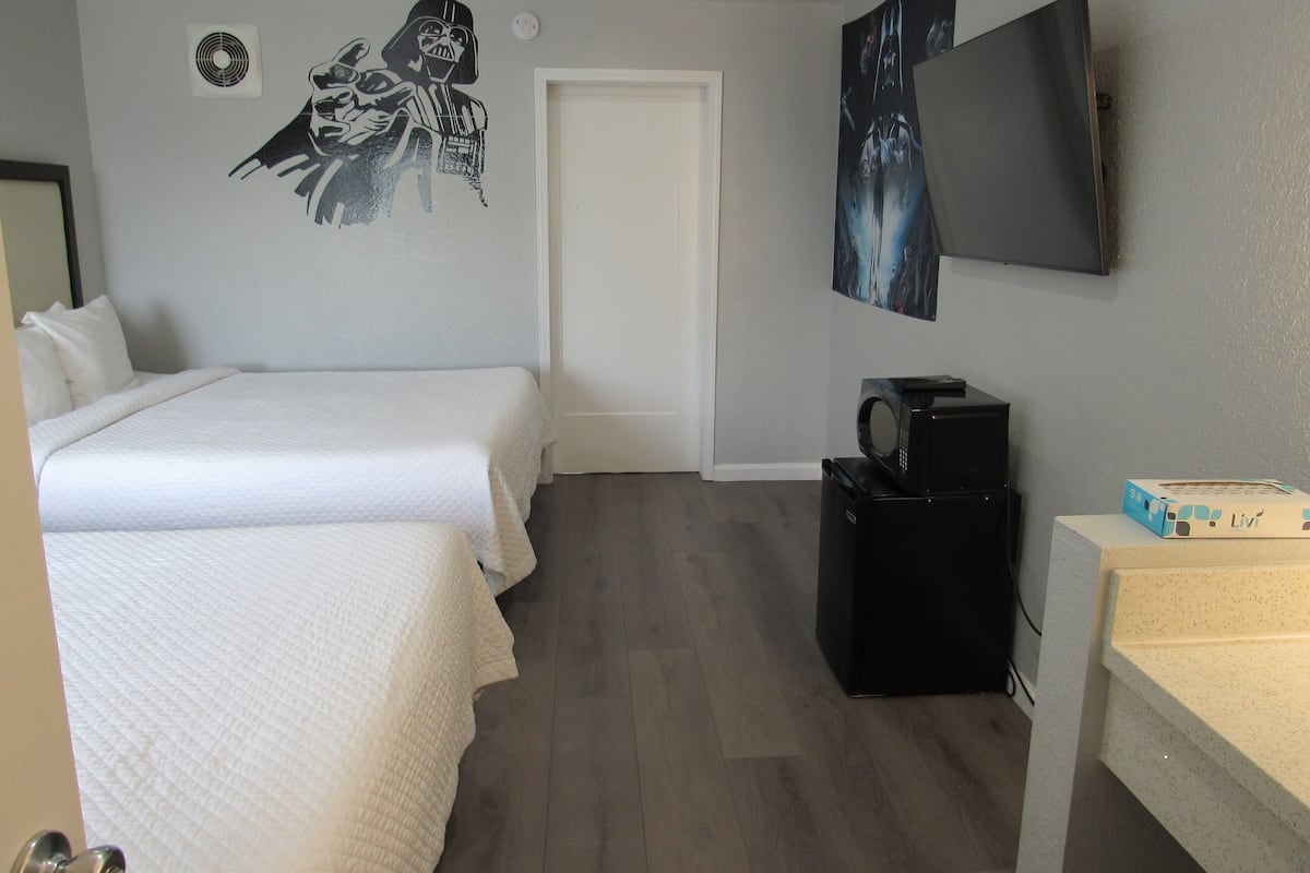 A hotel room with two beds, a microwave, a small refrigerator, a TV, and a wall with a Darth Vader poster.