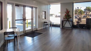 A hotel lobby with a reception desk, two chairs, a small table, and a large window offering a view of the street. - Capri Suites Anaheim (Anaheim)