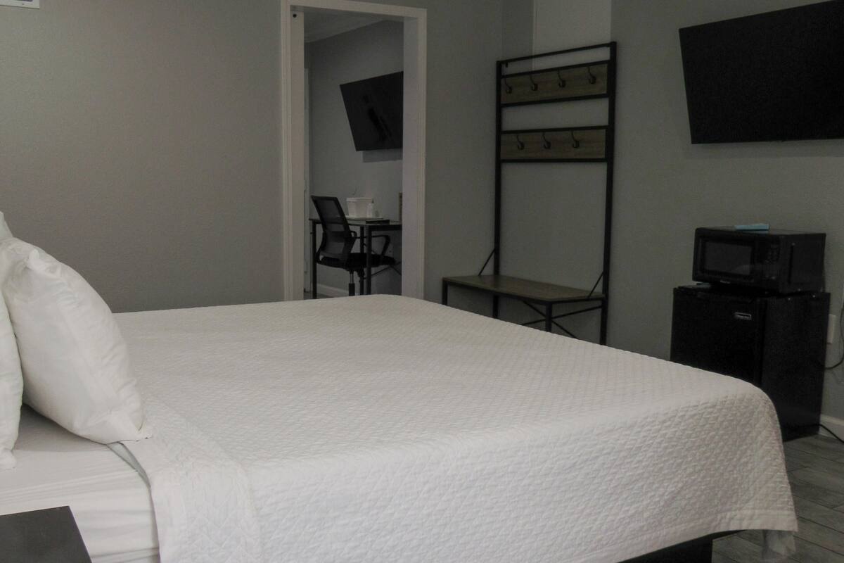 A hotel room with a bed, a desk, a chair, a television, and a microwave.