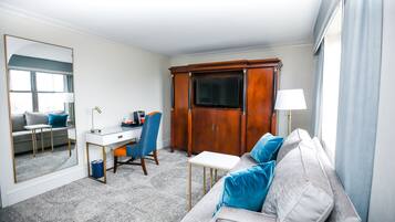 Et hotelværelse med sofa, skrivebord, stol, garderobeskab og fjernsyn.